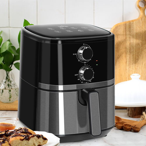 Black and silver air fryer on kitchen counter with white tiled wall and wooden cutting board in the background